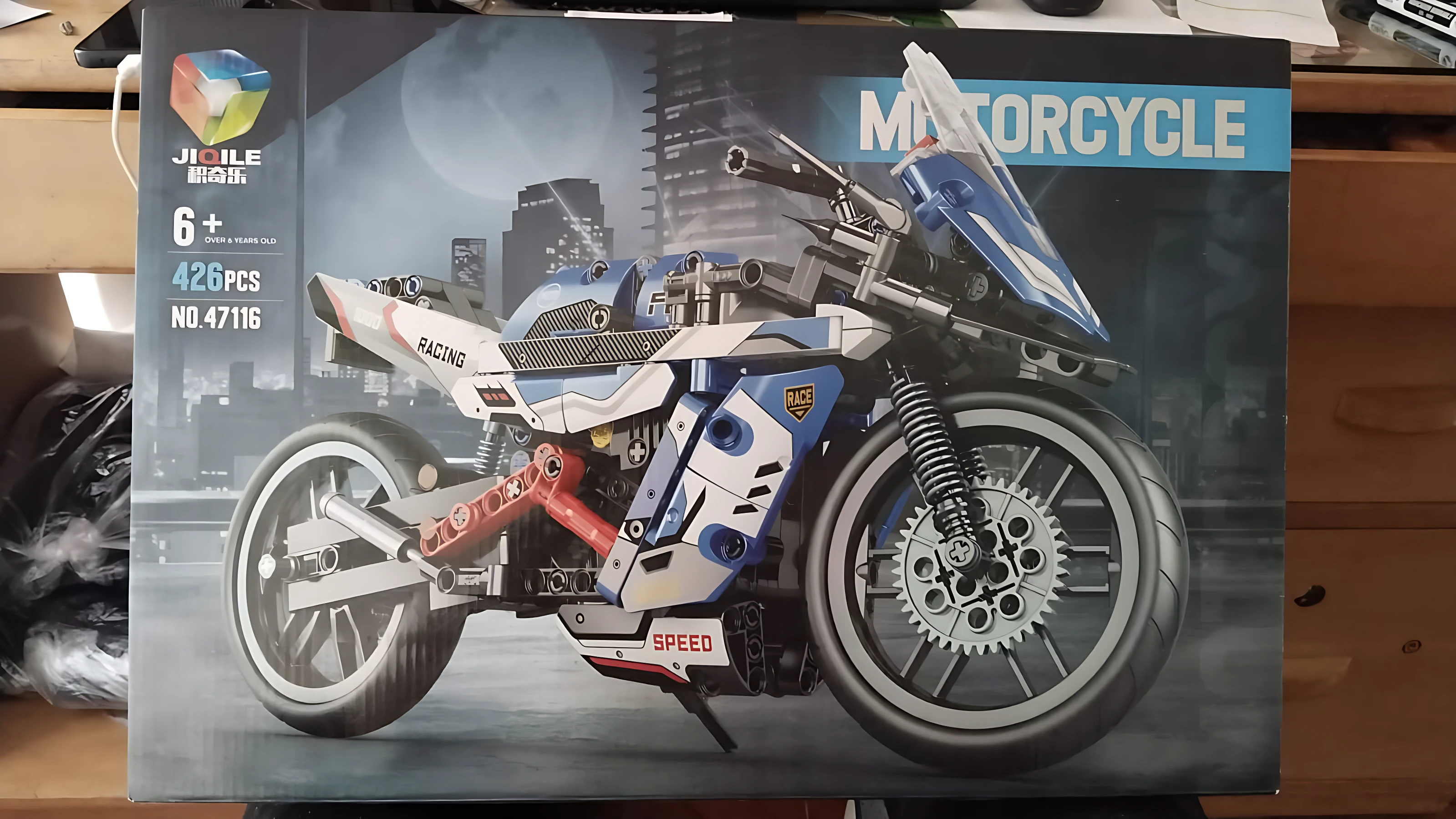 Caja de construcción de moto deportiva Jule Model, modelo 47116, con 426 piezas en colores blanco, azul y rojo, mostrando la motocicleta ensamblada en vista lateral sobre fondo urbano nocturno.