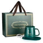 Termo eléctrico de cerámica verde con base calefactora, incluye taza y bandeja; presentación en bolsa de regalo con asas marrones.