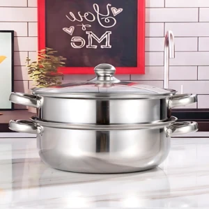 Olla vaporera de acero inoxidable con tapa de vidrio y dos niveles, sobre encimera blanca en cocina decorada.