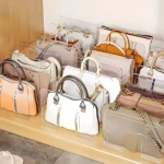 Organizador de bolsos transparente con divisiones, exhibiendo múltiples bolsos de colores y texturas sobre estantes de madera.