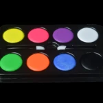 Paleta artística con ocho colores vibrantes, incluyendo amarillo, rosa, morado, blanco, verde, naranja, azul y negro, dispuestos en dos filas sobre base negra.