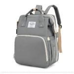 Pañalera morral gris con cambiador integrado, asas superiores y compartimentos laterales visibles.