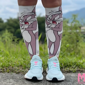 Pantorrilleras de compresión con diseño de Bugs Bunny en tonos rosados y blancos, usadas con zapatillas deportivas azules sobre césped.