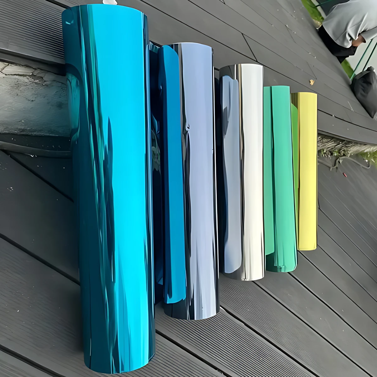 Set de dos rollos de papel polarizado para ventanas en colores azul, gris, blanco, verde y amarillo, dispuestos sobre superficie de madera.