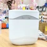 Papelera de cocina blanca con tapa y detalles grises, vista frontal sobre superficie de madera.
