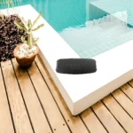 Parlante JBL Charge 5 negro sobre borde de piscina con plantas decorativas, ideal para uso al aire libre.