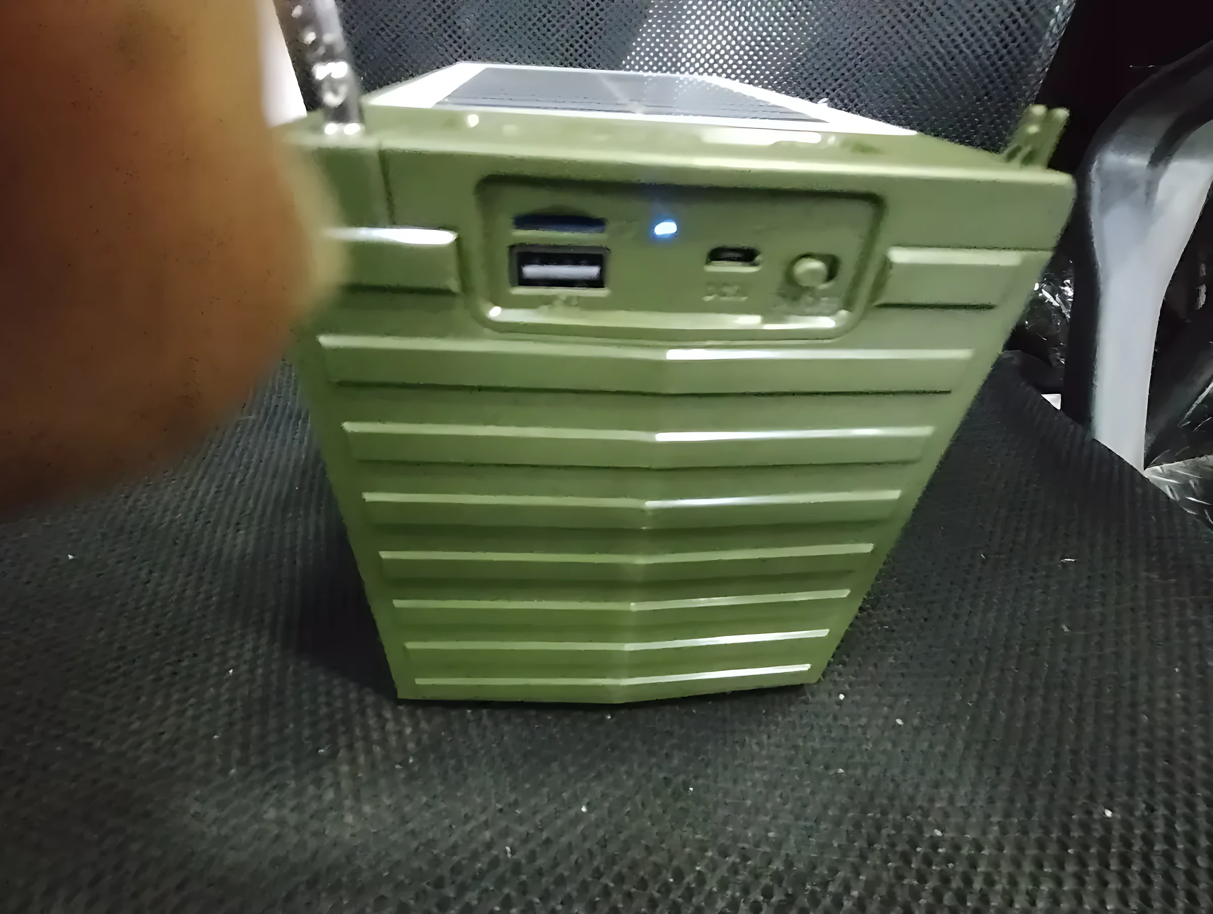 Parlante J-Ipok P818 color verde militar con panel solar en la parte superior, puertos USB y entrada de audio visibles en el panel trasero.