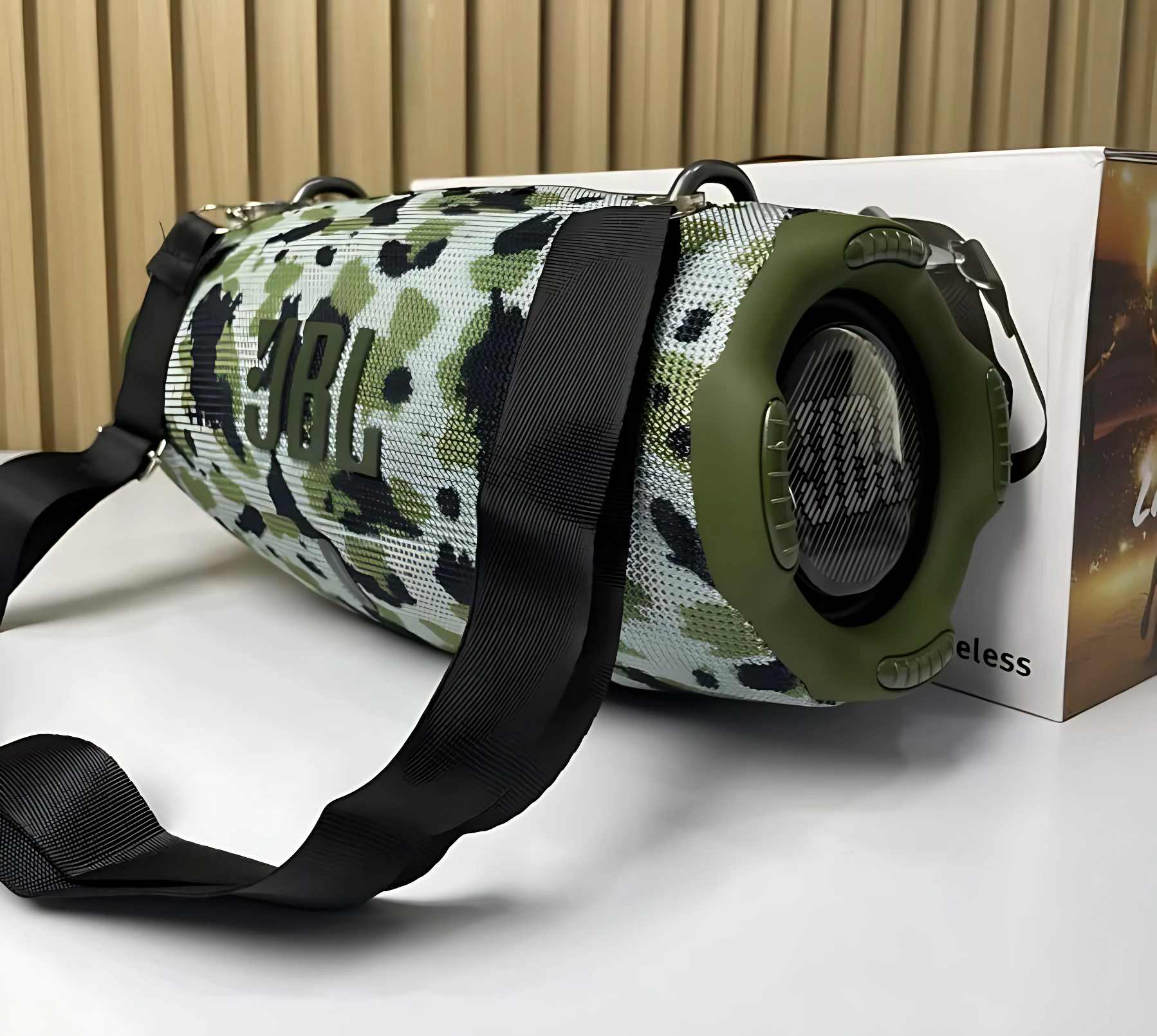 Altavoz JBL Xtreme 4 en patrón camuflaje verde y negro, con correa negra ajustable y caja blanca al fondo.