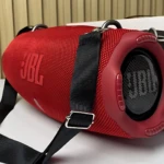 Altavoz JBL Xtreme 4 en color rojo con detalles negros, textura de malla y correa ajustable, mostrando la rejilla frontal y el logotipo en relieve.