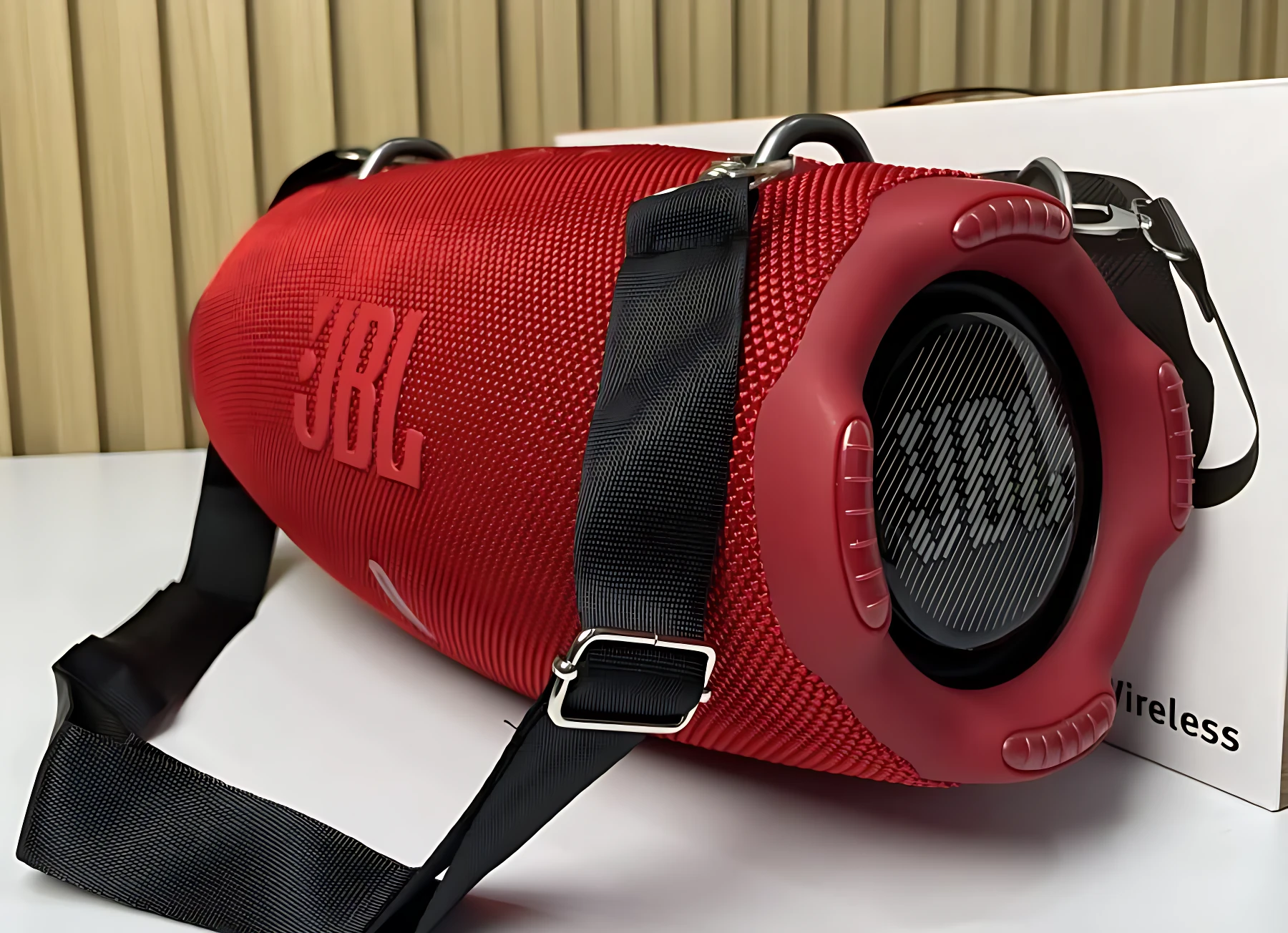 Altavoz JBL Xtreme 4 en color rojo con detalles negros, textura de malla y correa ajustable, mostrando la rejilla frontal y el logotipo en relieve.