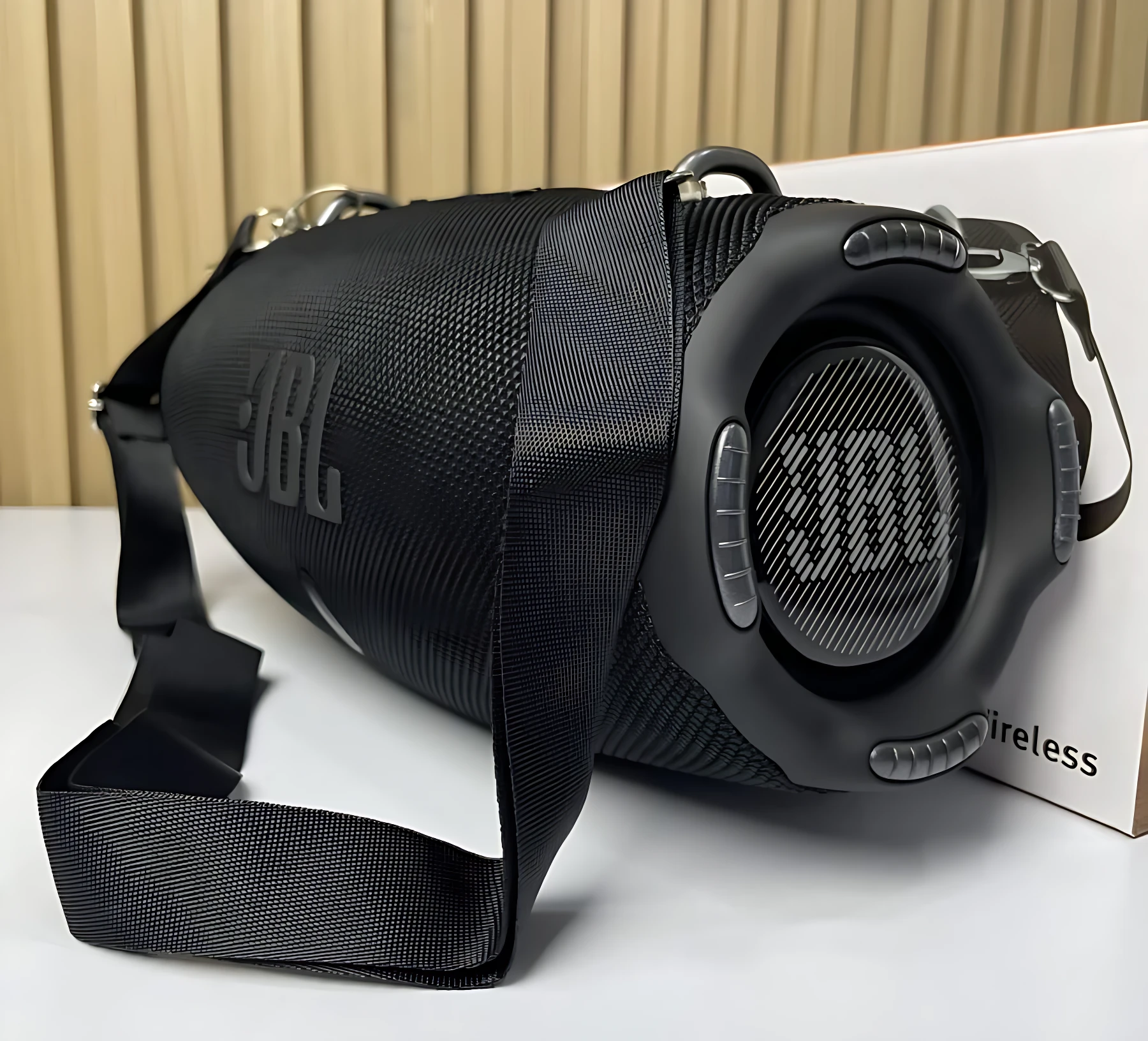 Altavoz JBL Xtreme 4 negro con correa de transporte, mostrando rejilla frontal y logotipo lateral sobre caja blanca.