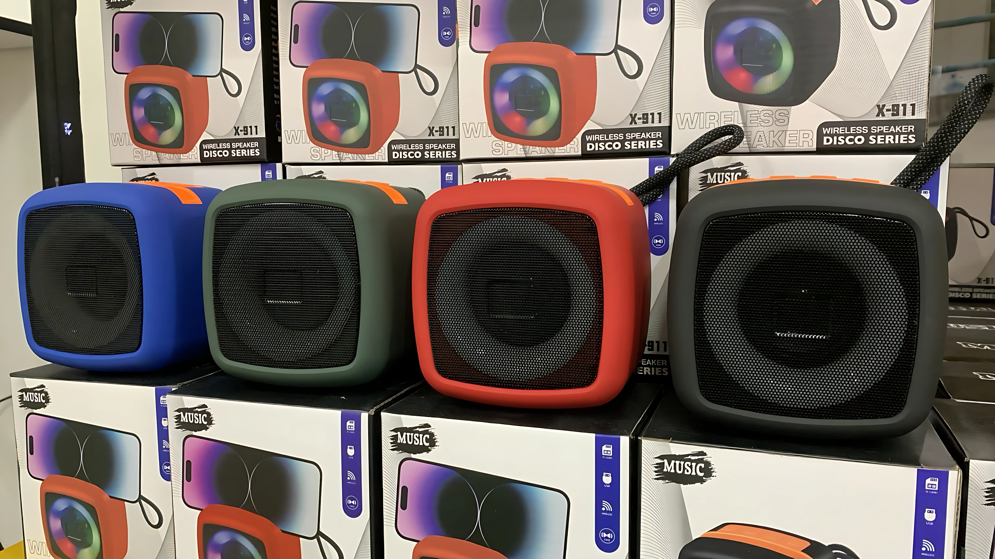 Cuatro parlantes Bluetooth X-911 en colores azul, verde, rojo y negro, exhibidos sobre cajas de su empaque original.