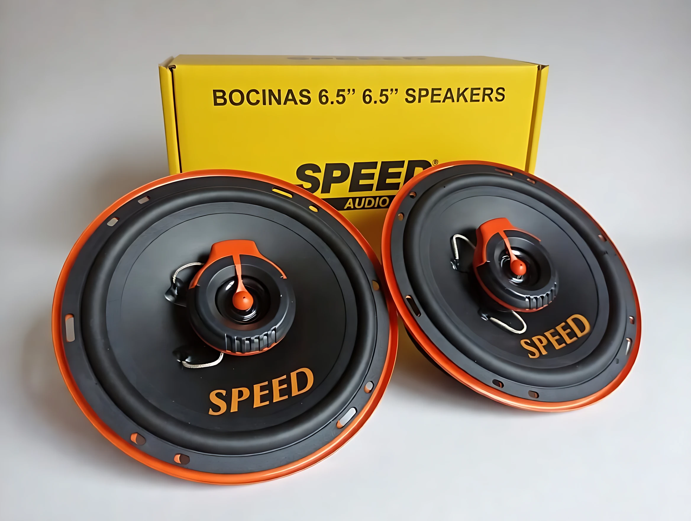 Parlantes automotrices Speed de 6.5 pulgadas, color negro con detalles naranjas, mostrando dos unidades frente a su caja amarilla con texto visible.