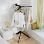 Perchero metálico árbol negro con perchas, sostiene blusa blanca, bolso beige y sombrero en habitación con luz natural.