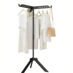 Perchero metálico árbol negro con perchas integradas, mostrando vestido blanco, blusas y bolso beige colgados. Base trípode estable.