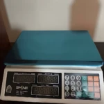 Báscula electrónica de mesa con plataforma azul y teclado numérico, marca SHINE, con pantalla digital para peso, precio unitario y total.