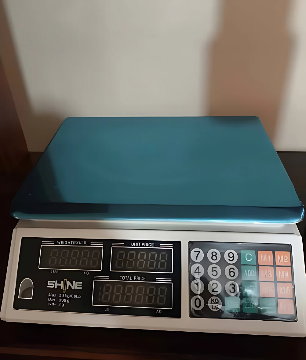 Báscula electrónica de mesa con plataforma azul y teclado numérico, marca SHINE, con pantalla digital para peso, precio unitario y total.