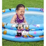 Niña riendo en piscina inflable azul con Mickey Mouse, Donald y Minnie, sobre césped verde.