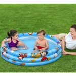 Piscina inflable azul con Mickey Mouse, tres anillos y dibujos de personajes. Niño y niña jugando dentro, mujer acostada al lado en césped verde.