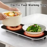 Plato eléctrico calentador con dos zonas de calefacción, superficie negra con anillos rojos visibles, sobre mesa blanca; una persona coloca olla con comida y otro plato con ensalada verde encima.