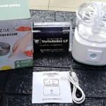 Procesador de alimentos inalámbrico blanco con caja, manual y cable de carga sobre superficie oscura texturizada.