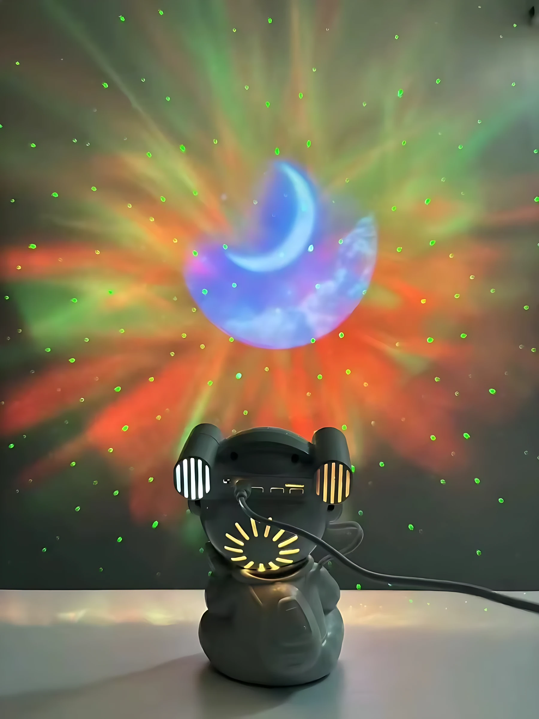 Proyector de noche en forma de astronauta gris, con luces multicolores y estrellas proyectadas en la pared. Incluye parlante integrado y diseño amigable para niños.