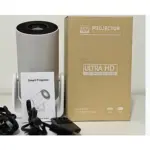 Proyector LED Y300 en color gris, acompañado de su caja de cartón beige, manual, cables y control remoto sobre superficie blanca.