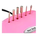 Pulidor eléctrico de uñas rosa con seis accesorios metálicos dispuestos en ranuras, cable negro visible y etiqueta que indica Nail Drill.