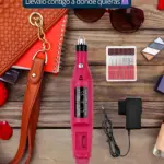 Pulidor de uñas eléctrico en color rosa con cargador y accesorios incluidos, sobre superficie de madera con bolso y accesorios de belleza alrededor.