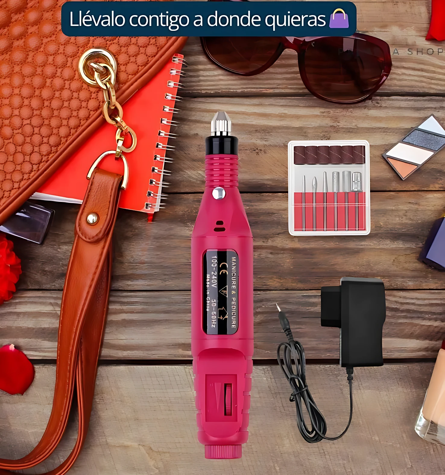 Pulidor de uñas eléctrico en color rosa con cargador y accesorios incluidos, sobre superficie de madera con bolso y accesorios de belleza alrededor.
