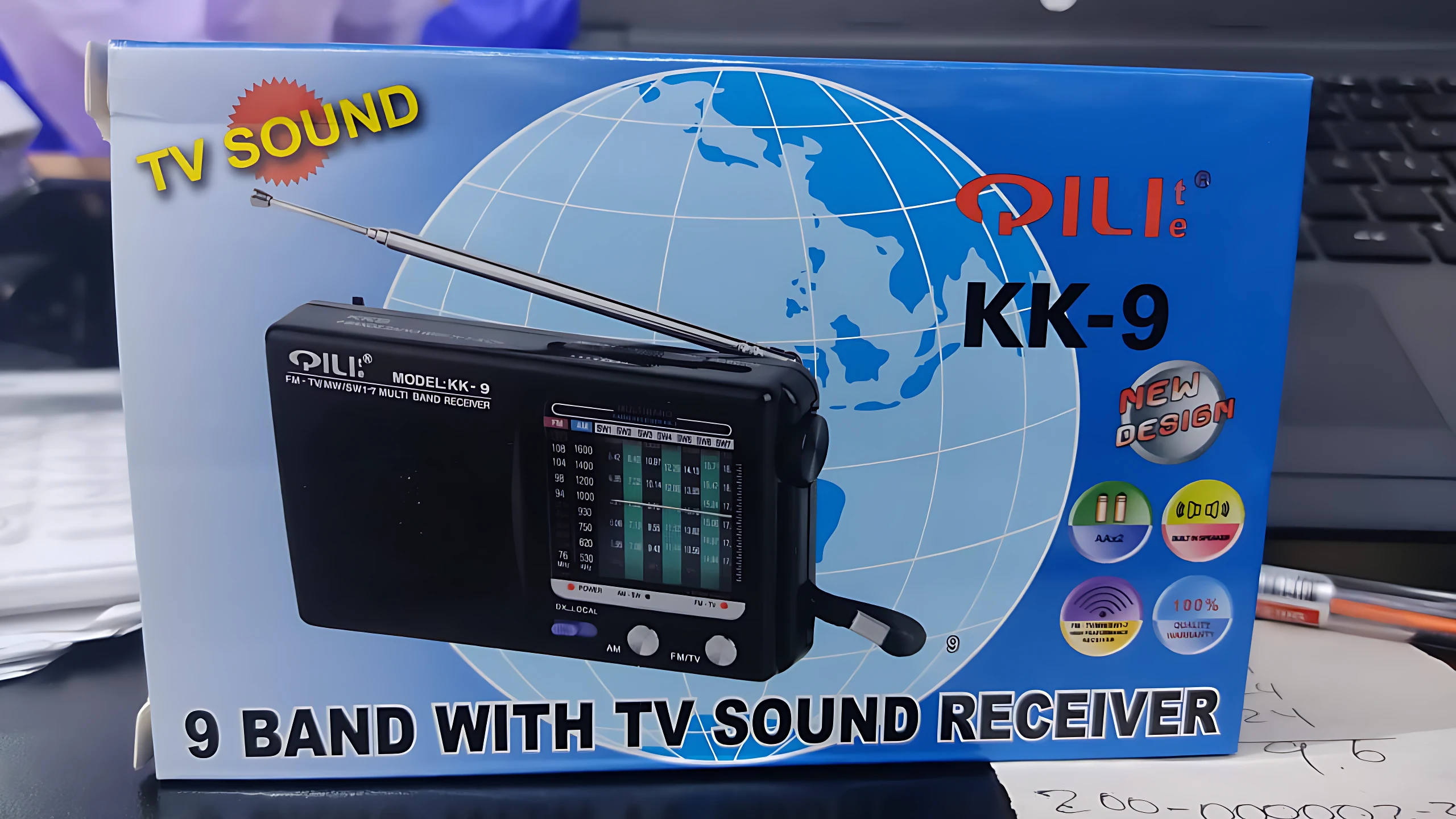 Radio portátil Pili KK-9 en caja azul con fondo de globo terráqueo, antena telescópica extendida y pantalla digital visible. Incluye receptor de TV y sonido.