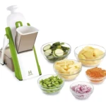 Rallador mandoline verde con mango seguro, mostrando seis recipientes de vidrio con vegetales cortados: calabacín, papas, zanahorias, cebolla morada, pimientos verdes y manzanas.