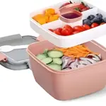 Recipiente portátil para ensalada en color rosa con tapa gris, mostrando dos niveles: uno con vegetales frescos y otro con frutas y aderezo, diseñado para mantener ingredientes separados.