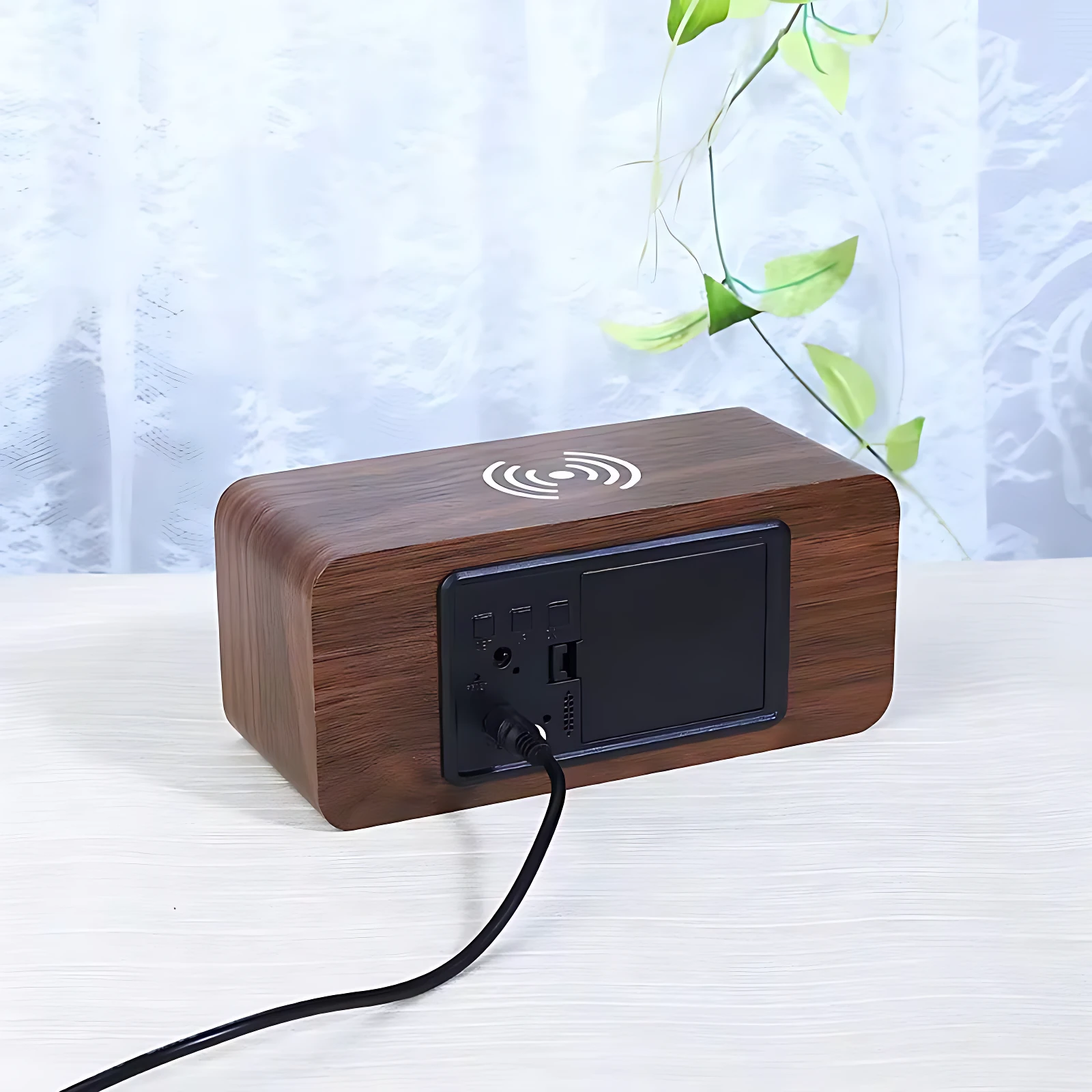 Reloj despertador de madera con carga inalámbrica, enchufes y puerto USB en panel trasero, conectado por cable negro sobre superficie blanca.