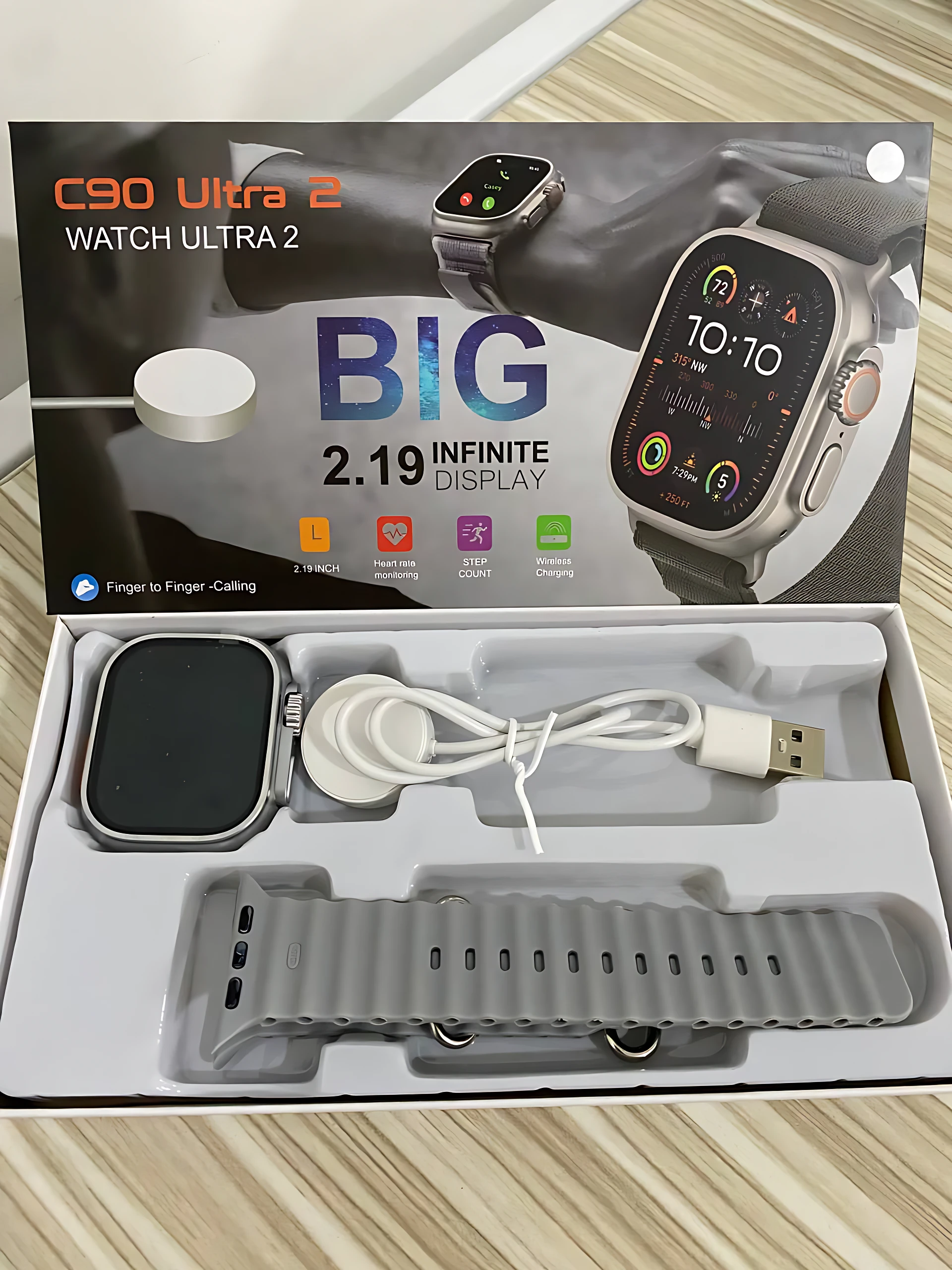 Smartwatch C90 Ultra 2 en caja abierta, mostrando reloj negro, correa gris, cable de carga y auriculares. Caja con del dispositivo y texto "BIG 2.19 INFINITE DISPLAY".