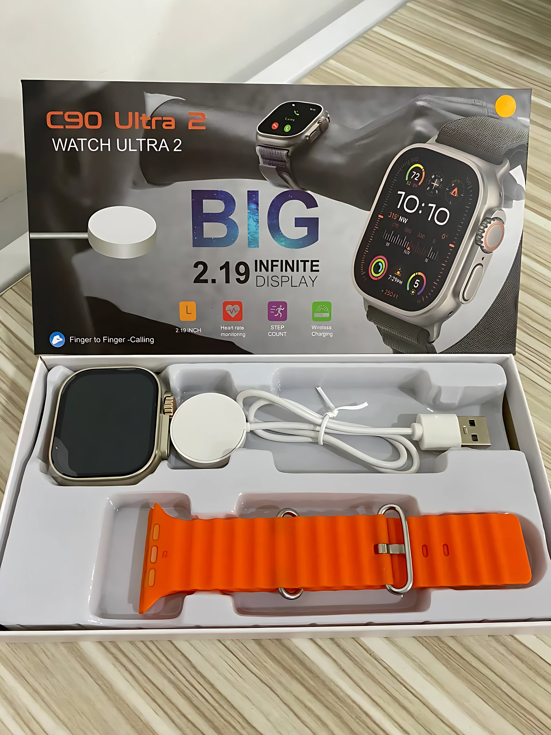 Smartwatch C90 Ultra 2 con pantalla de 2.19 pulgadas, caja abierta mostrando reloj con correa naranja, cargador inalámbrico y cable USB.