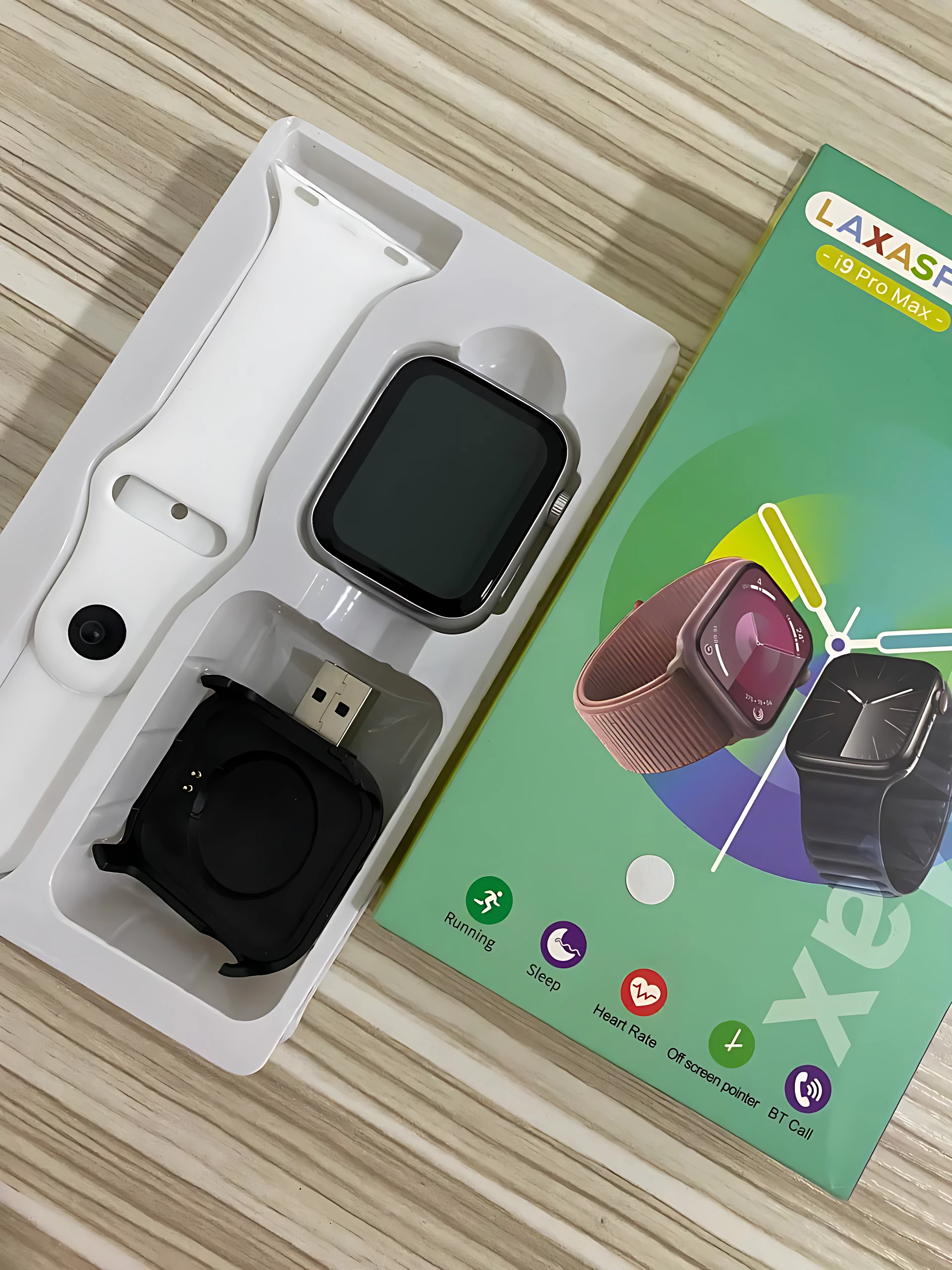 Pack de reloj inteligente I9 Pro Max en caja abierta, mostrando pulsera blanca, cargador USB y dispositivo principal con pantalla apagada, sobre fondo de madera.