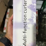 Rizador portátil compacto LR-288 en caja rectangular con diseño floral en tonos lavanda y blanco, sostenido en mano.