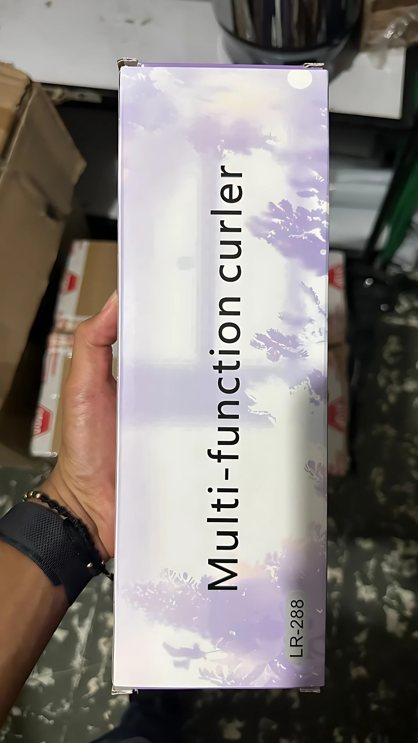 Rizador portátil compacto LR-288 en caja rectangular con diseño floral en tonos lavanda y blanco, sostenido en mano.