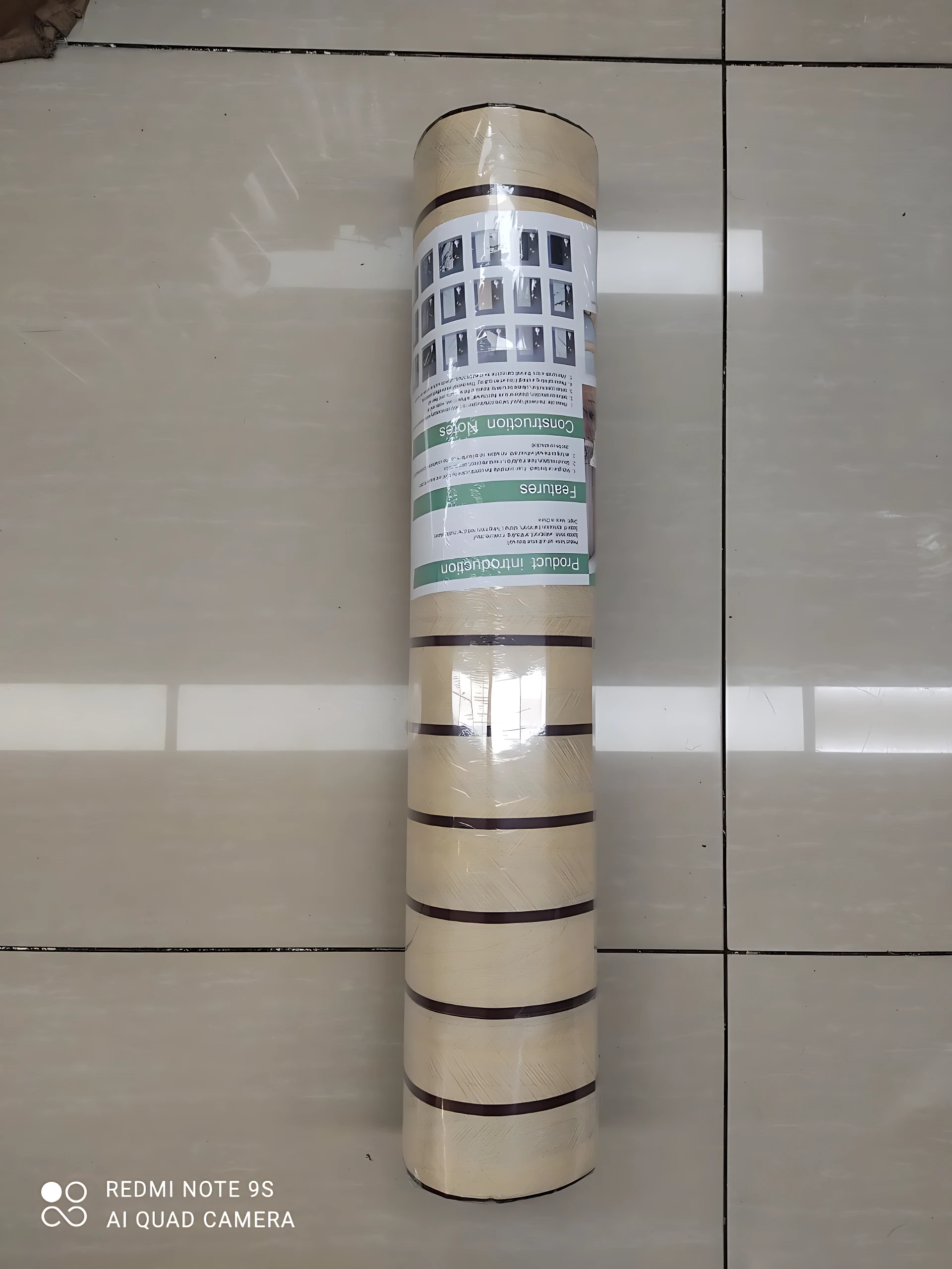 Rollo adhesivo pared acolchonado de alta resistencia, color beige con franjas oscuras, envuelto en plástico transparente y con etiqueta informativa visible.