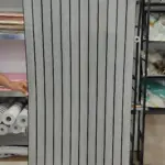 Rollo adhesivo pared acolchado con diseño de rayas verticales blancas y negras, mostrando textura y acabado listo para instalación.