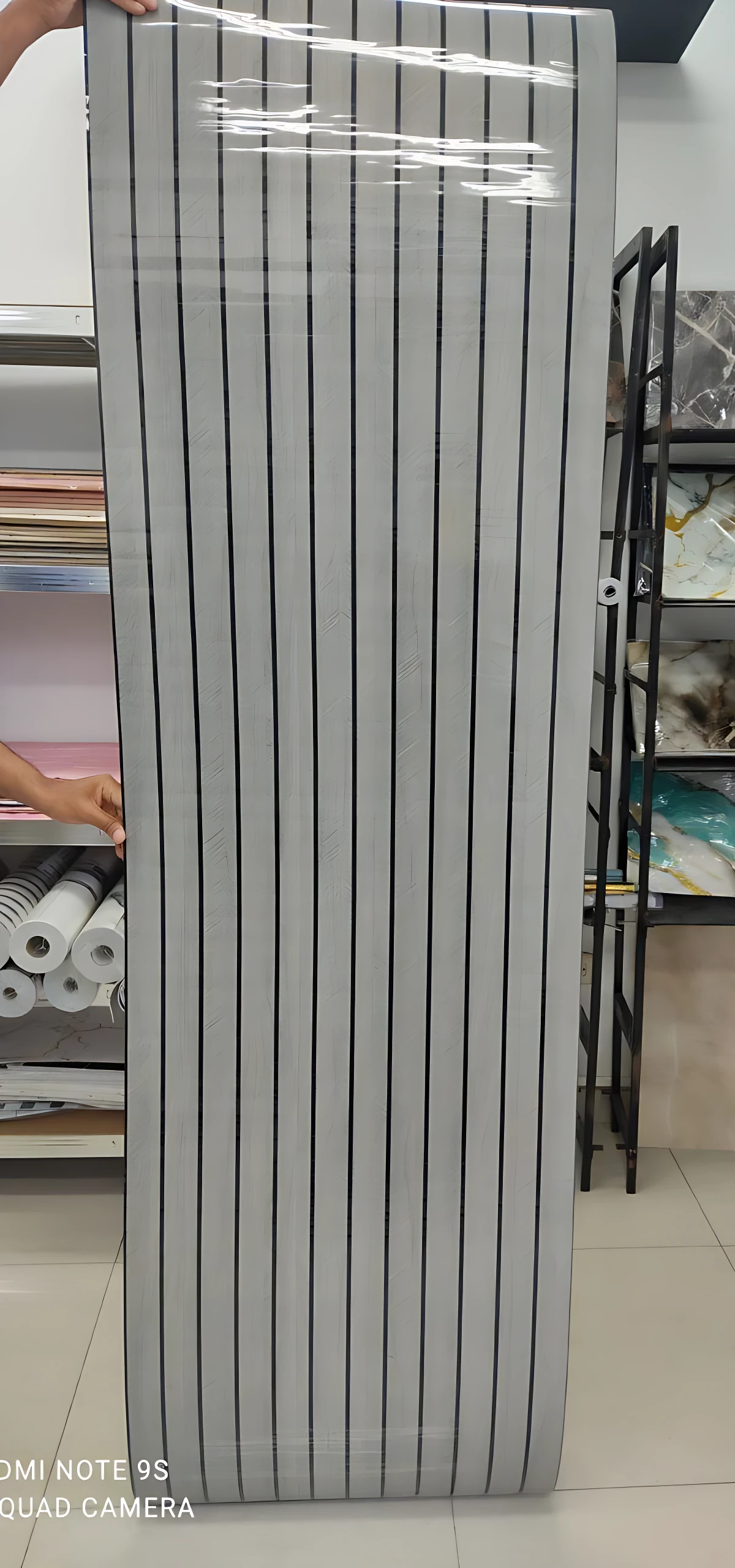 Rollo adhesivo pared acolchado con diseño de rayas verticales blancas y negras, mostrando textura y acabado listo para instalación.