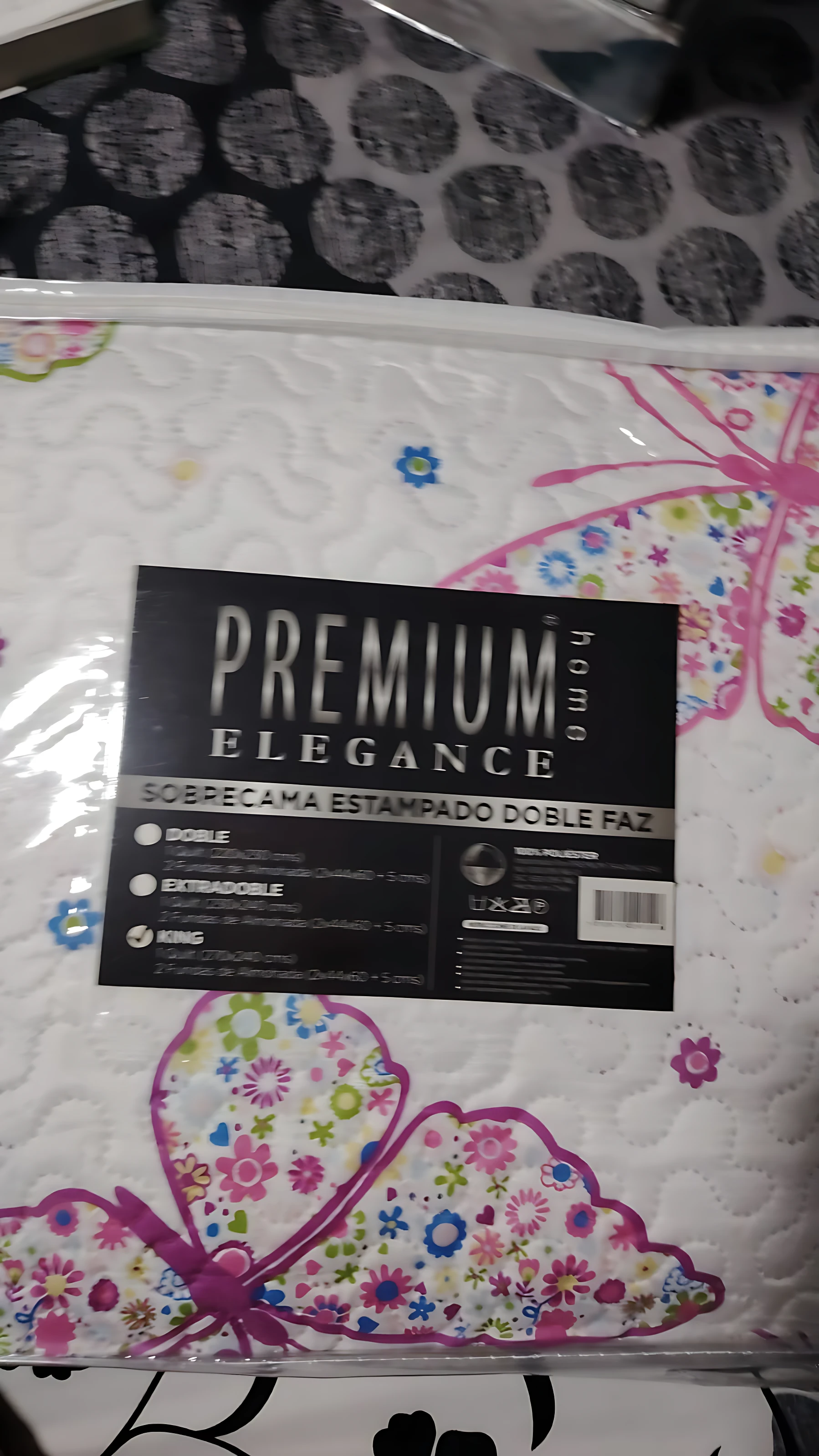 Colcha estampada floral doble faz, con diseño de mariposas multicolores y etiqueta visible que indica tallas doble y extra grande.