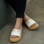 Sandalia Capella Prada en color crema con suela beige, vista desde arriba mostrando el logo dorado y el diseño de tiras anchas.