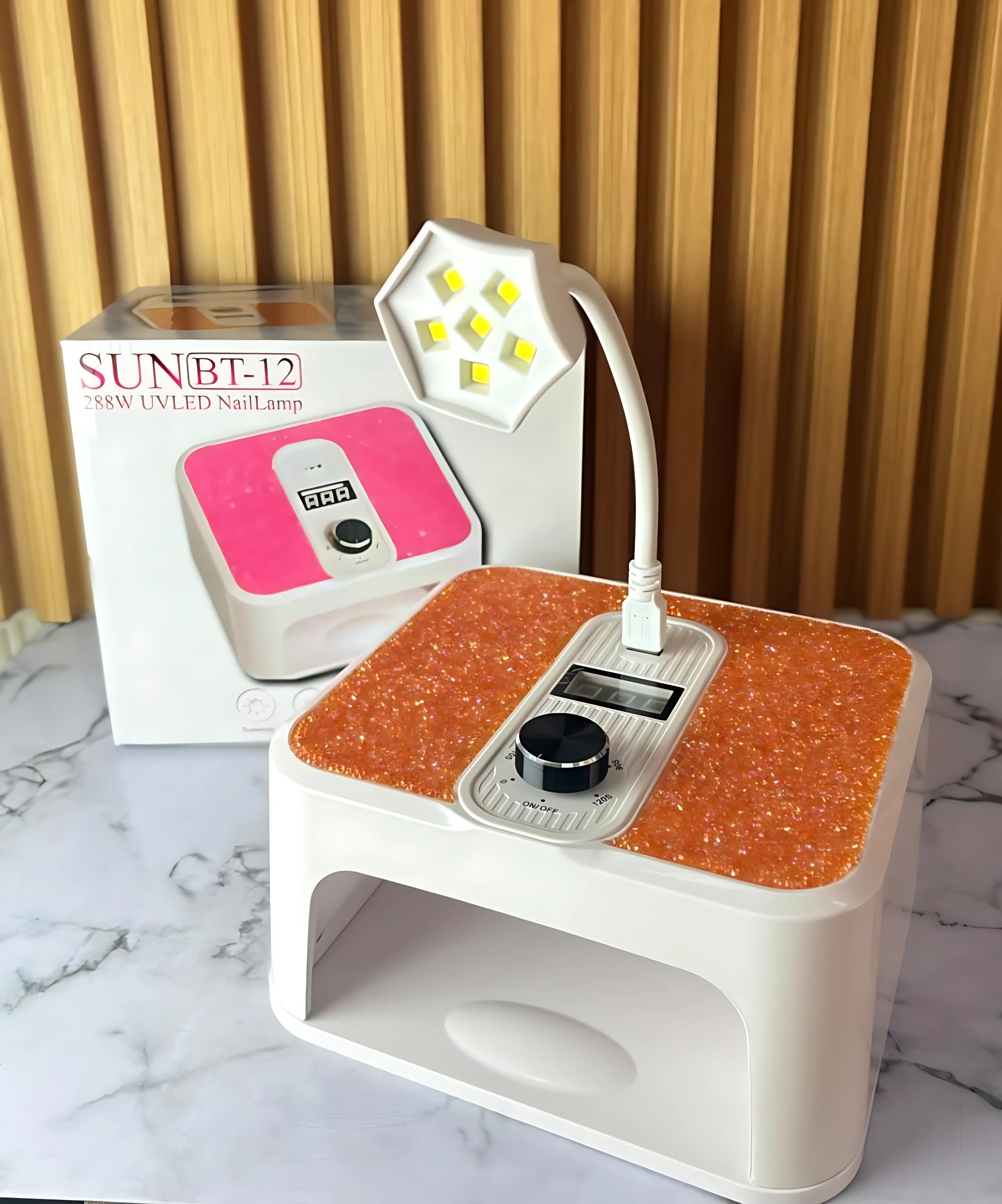 Lámpara LED UV SUNBT-12 con base naranja texturizada y panel de control digital, junto a su caja original. Ideal para secado rápido de esmaltes y pedicura.