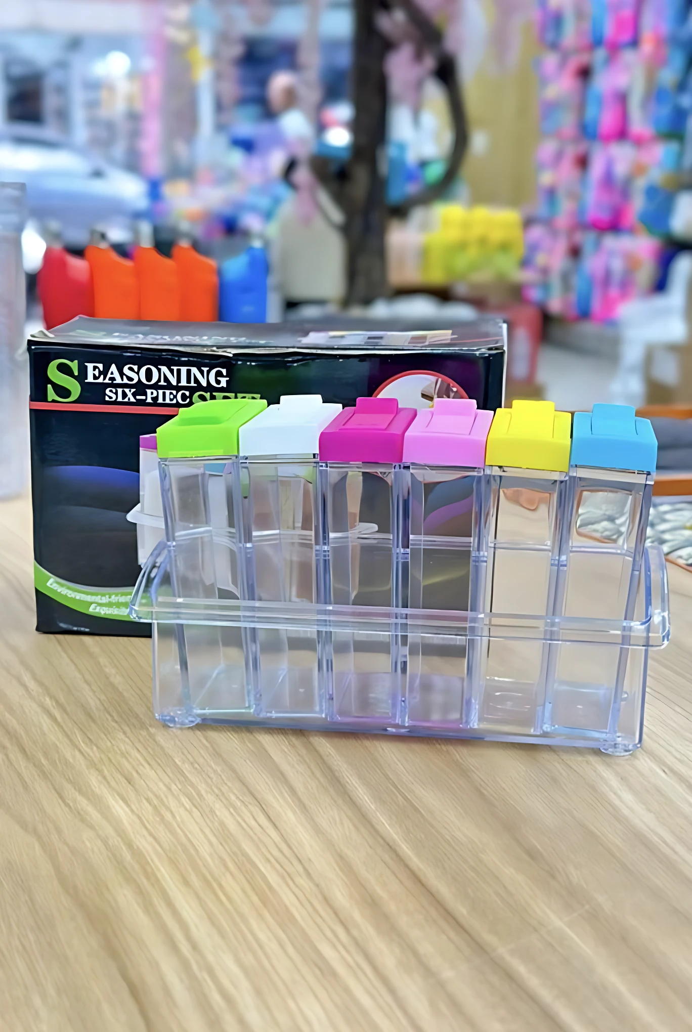 Organizador de especias transparente con seis compartimentos, tapa de colores y caja de presentación visible.