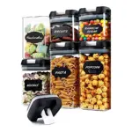 Set de seis contenedores herméticos transparentes con tapas negras, etiquetados con nombres de alimentos como galletas, pasta y palomitas.