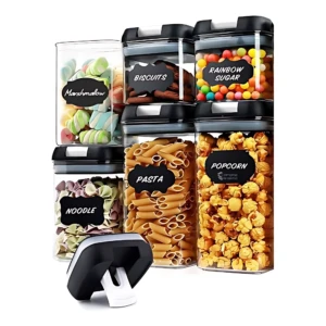 Set de seis contenedores herméticos transparentes con tapas negras, etiquetados con nombres de alimentos como galletas, pasta y palomitas.