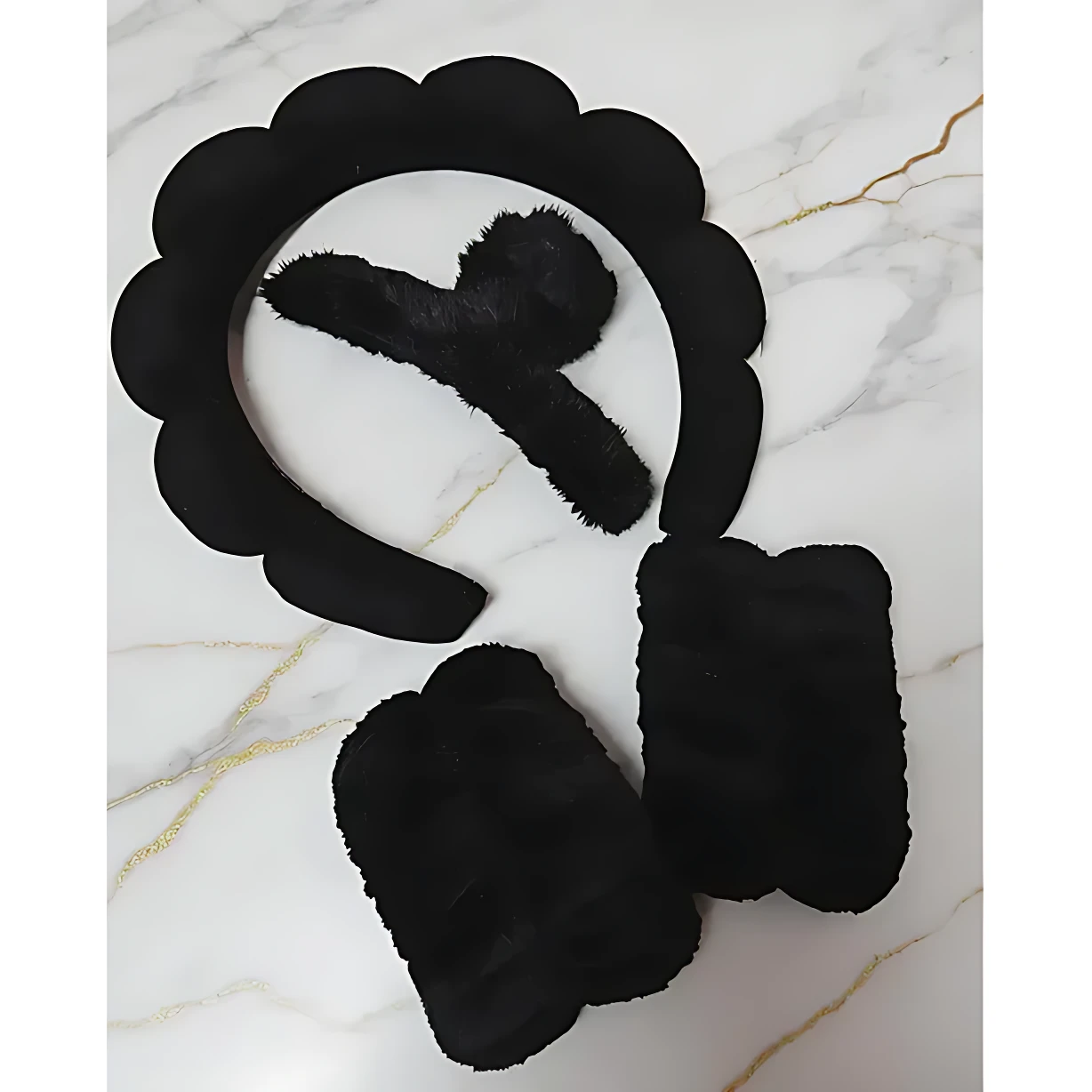 Set de diadema y accesorios negros con textura suave, sobre fondo de mármol blanco con vetas doradas. Incluye diadema con borde ondulado, dos paños rectangulares y un paño triangular, todos en color negro.