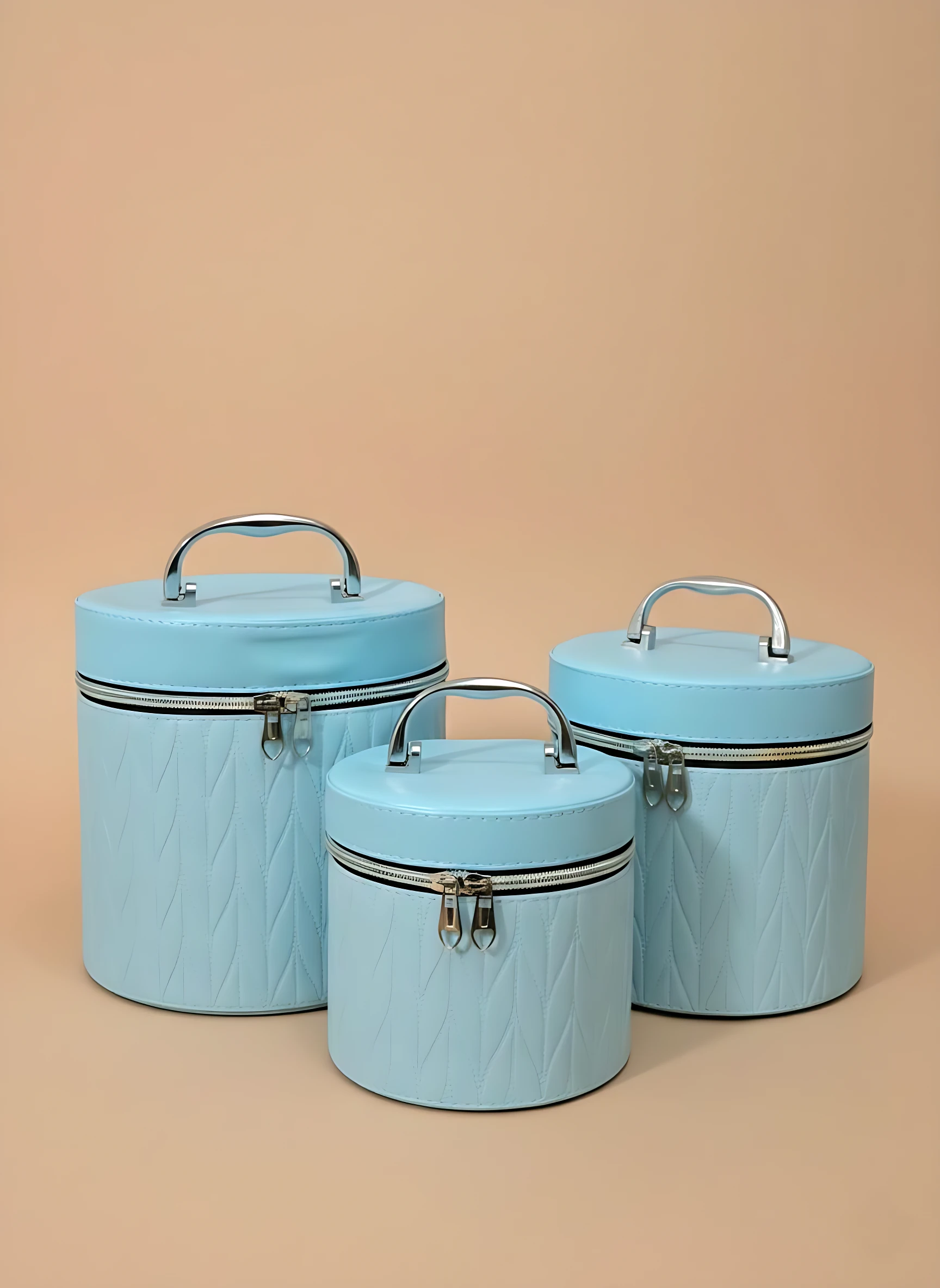 Set de tres neceseres circulares en azul claro con textura de rombos, cierre metálico y asa superior, ideales para organizar maquillaje y viajes.